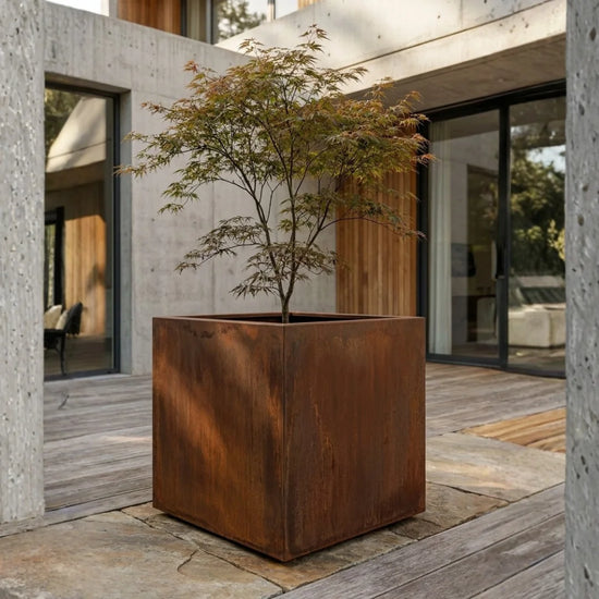 Steelart CUBE kubo formos metalinis lauko vazonas natūralios plieno spalvos prie modernaus namo terasos
